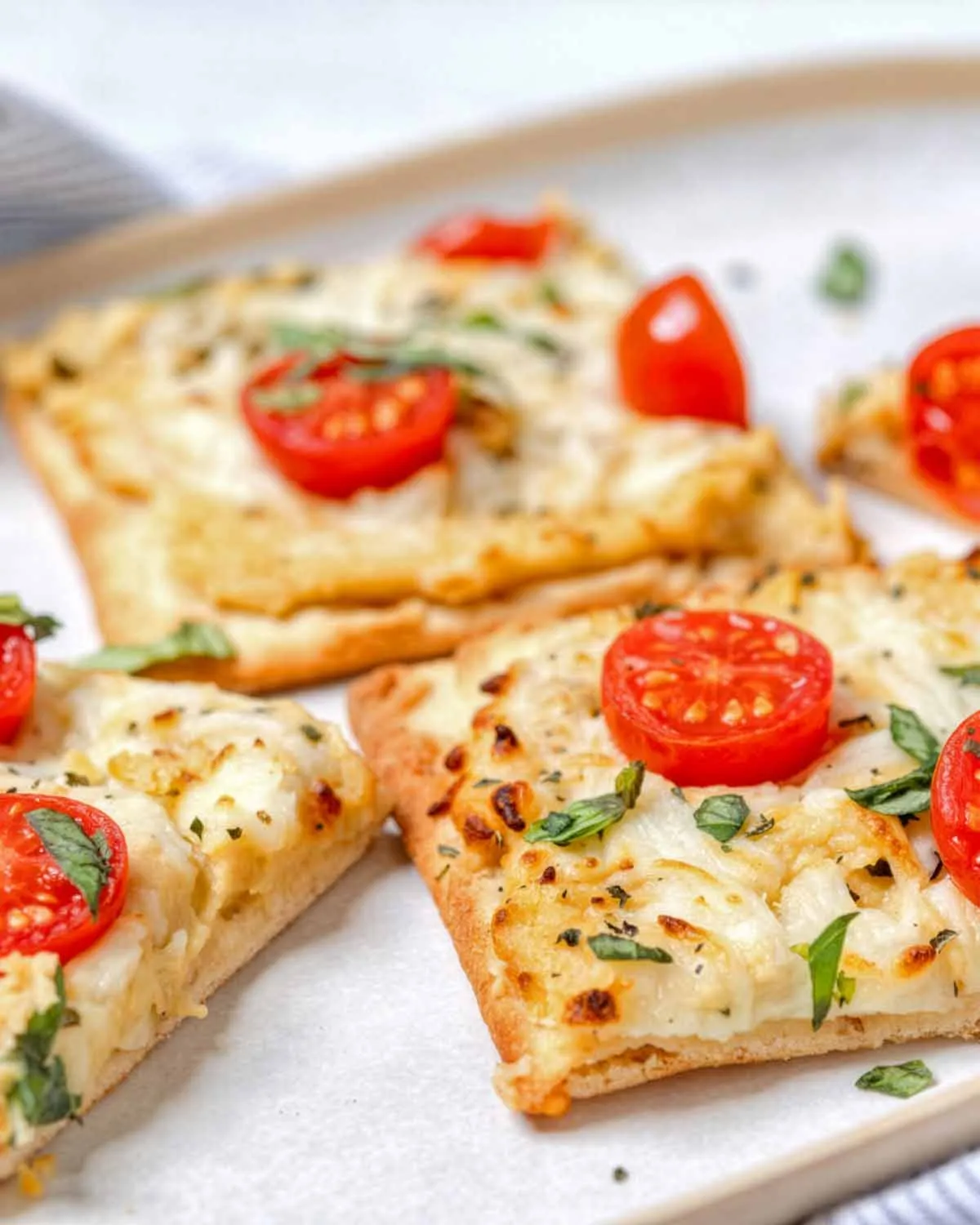 Close up of cheese flatbread on plate with cherry tomatoes and herbs