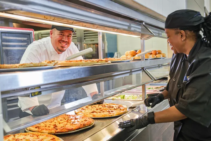 a chef peeks out from behind the pizza line